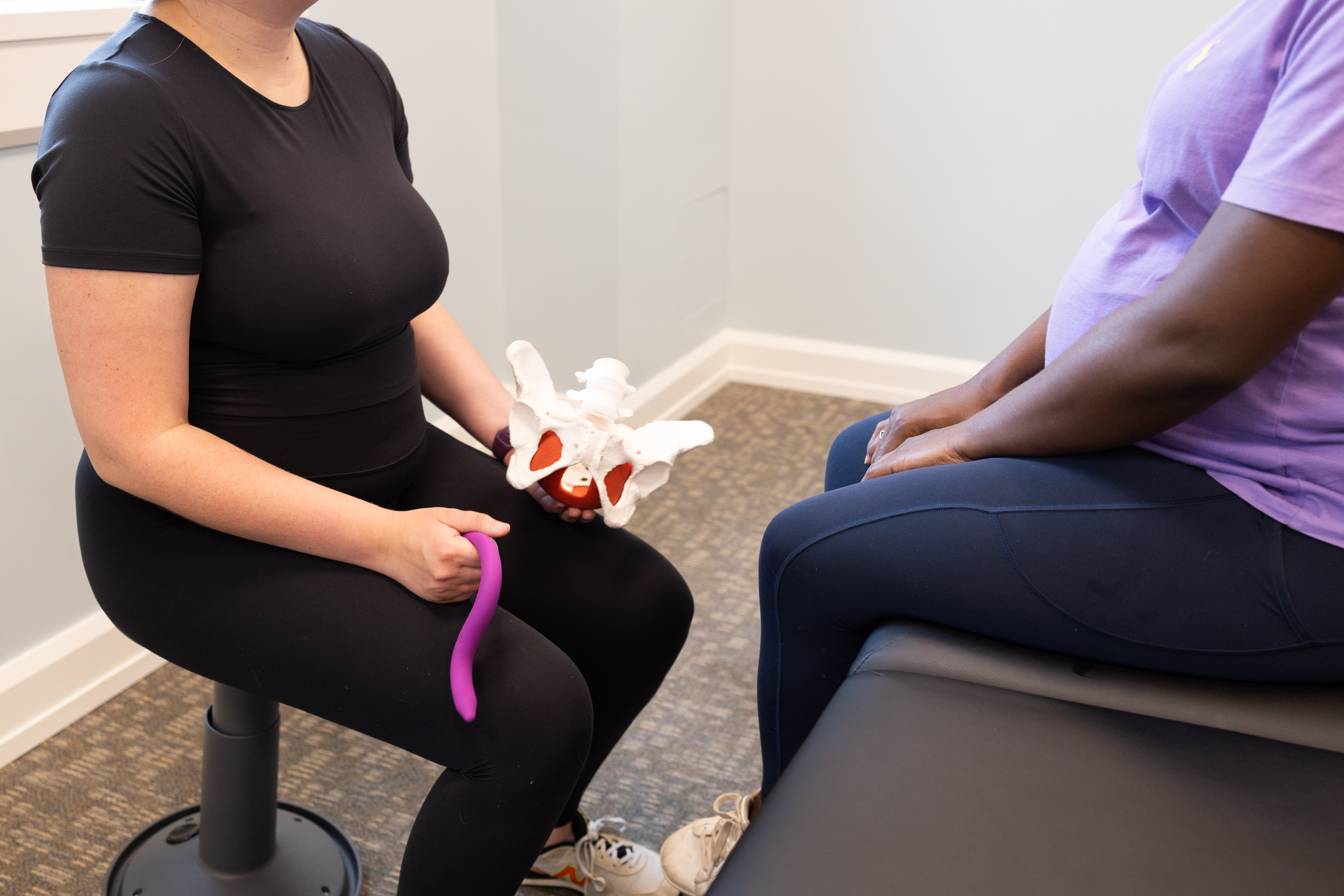 A physical therapist holds a model of a pelvis and a tool used in pelvic floor PT.